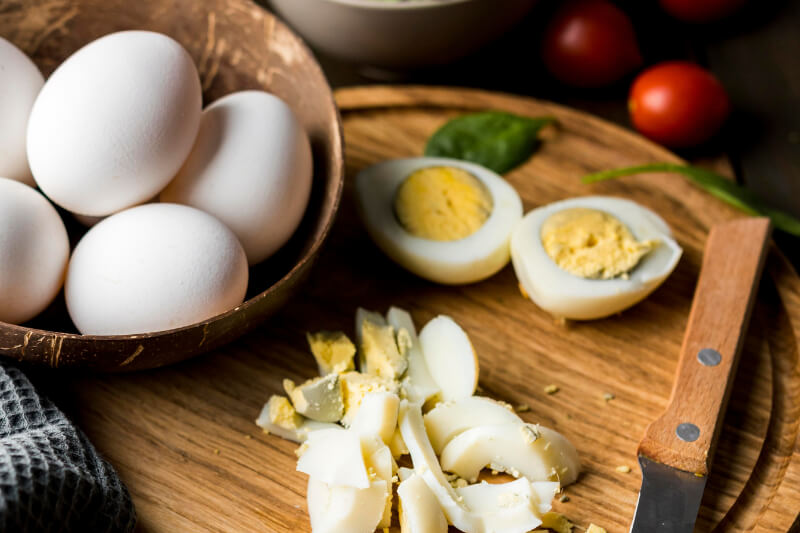 Vista superior de huevos de diferentes calibres, huevo entero, huevo roto con clara y yema visibles, huevo duro cortado por la mitad – ilustración del contenido de proteínas de un huevo.
